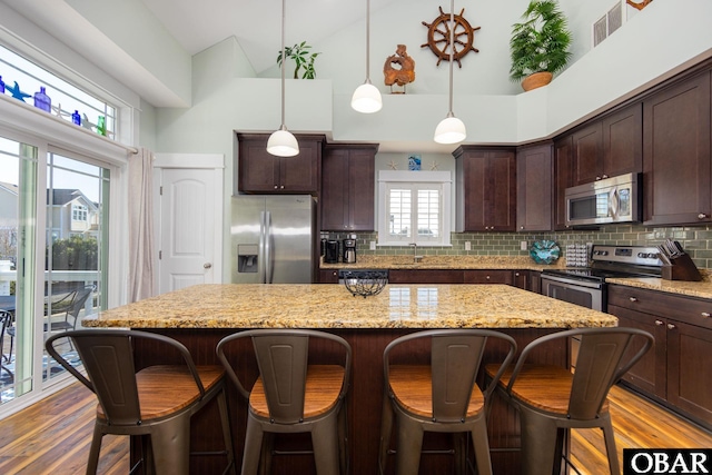 kitchen featuring tasteful backsplash, wood finished floors, a center island, stainless steel appliances, and a sink