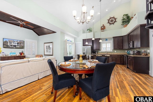 dining area with ceiling fan with notable chandelier, high vaulted ceiling, and wood finished floors