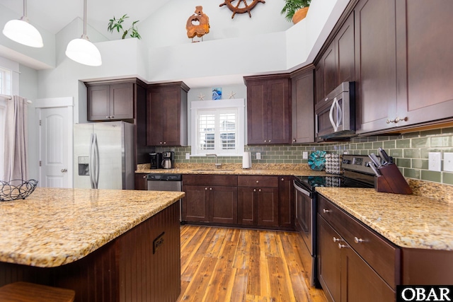 kitchen with light wood-style flooring, a sink, light stone countertops, stainless steel appliances, and backsplash