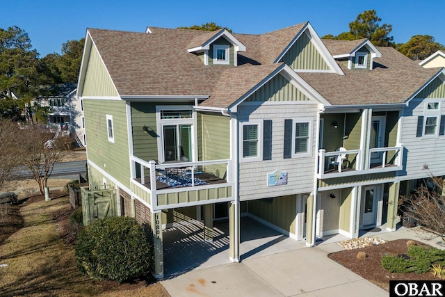 view of front of house featuring a carport, a shingled roof, a balcony, and driveway