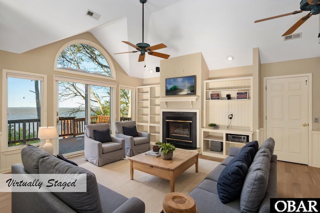 living room featuring a water view, visible vents, wood finished floors, and a glass covered fireplace