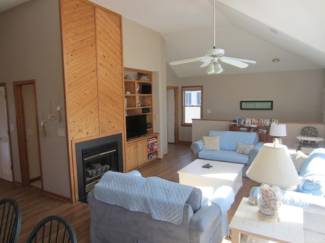 living area featuring dark wood-style floors, a glass covered fireplace, ceiling fan, and high vaulted ceiling