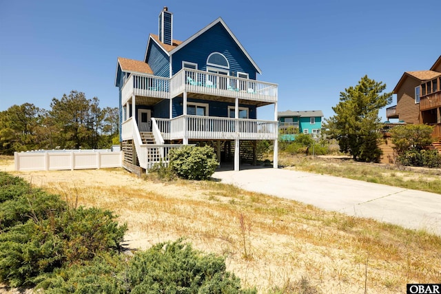 raised beach house with a balcony, a chimney, and fence