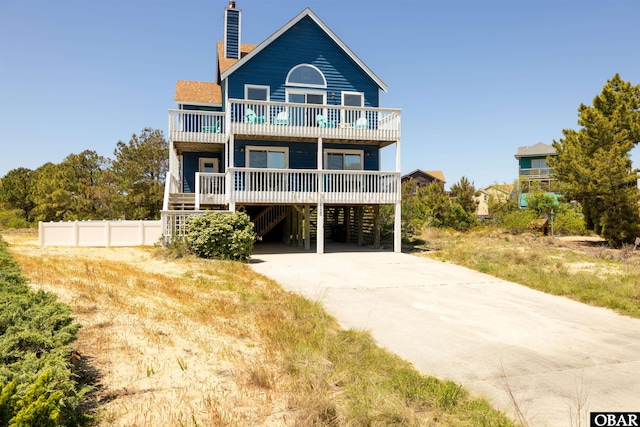 back of house with driveway, a carport, a chimney, and a balcony