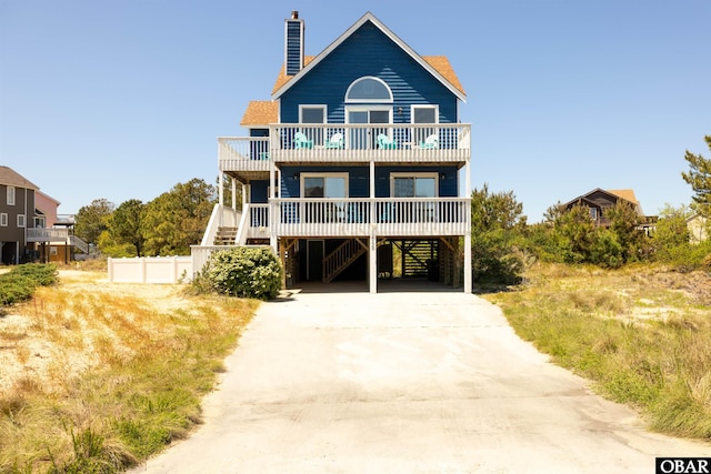 view of front of property featuring a chimney, a balcony, a carport, driveway, and stairs