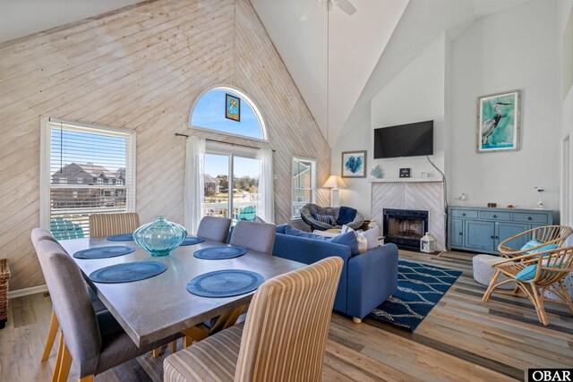 dining area featuring high vaulted ceiling, a tiled fireplace, and light wood-style flooring