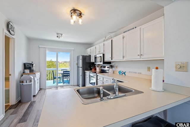 kitchen with white cabinets, wood finished floors, stainless steel appliances, light countertops, and a sink