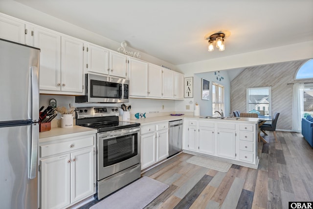 kitchen with white cabinets, appliances with stainless steel finishes, a peninsula, light countertops, and a sink