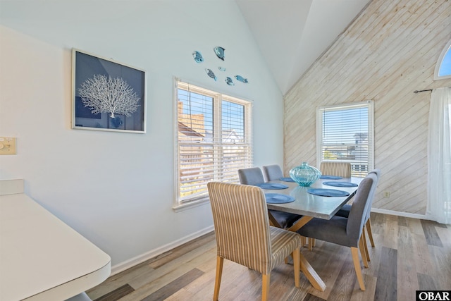 dining room with high vaulted ceiling, plenty of natural light, baseboards, and wood finished floors