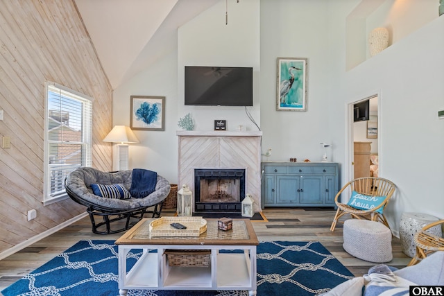 living area with wood walls, a fireplace, high vaulted ceiling, and wood finished floors