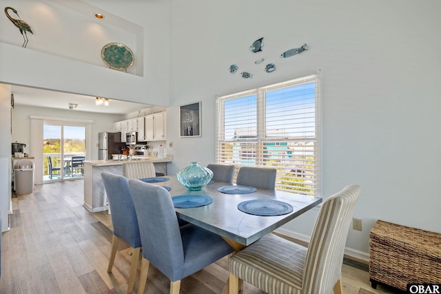 dining space featuring a towering ceiling, light wood-style floors, and baseboards