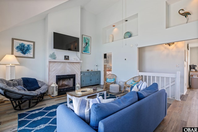 living area with high vaulted ceiling, a tiled fireplace, and wood finished floors