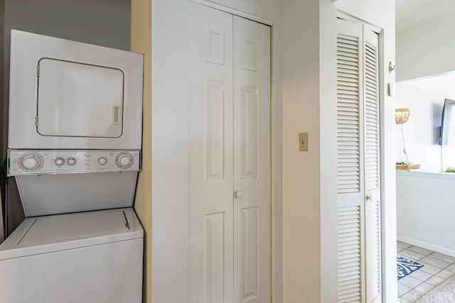 laundry area with stacked washer and dryer, baseboards, light tile patterned floors, and laundry area