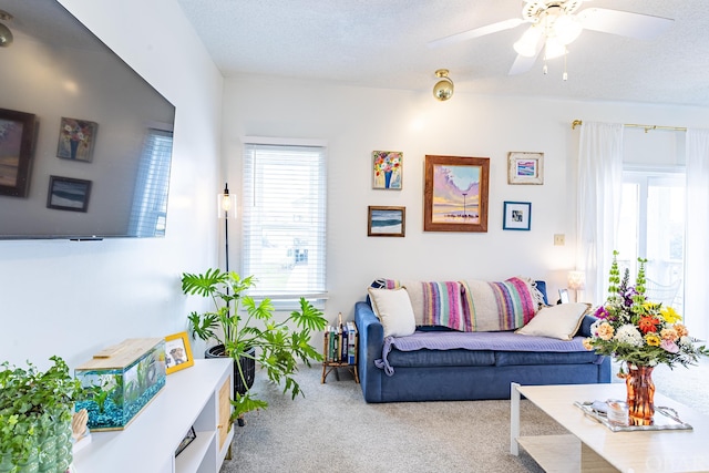 living area with light carpet, a ceiling fan, and a textured ceiling