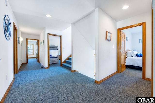 hall featuring dark colored carpet, baseboards, recessed lighting, and stairs