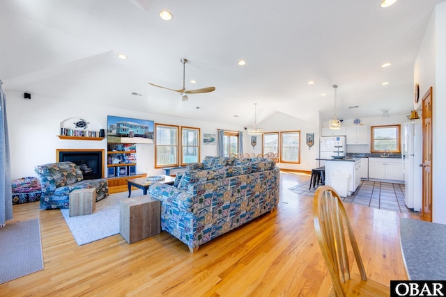 living room with recessed lighting, light wood-style flooring, vaulted ceiling, and a glass covered fireplace