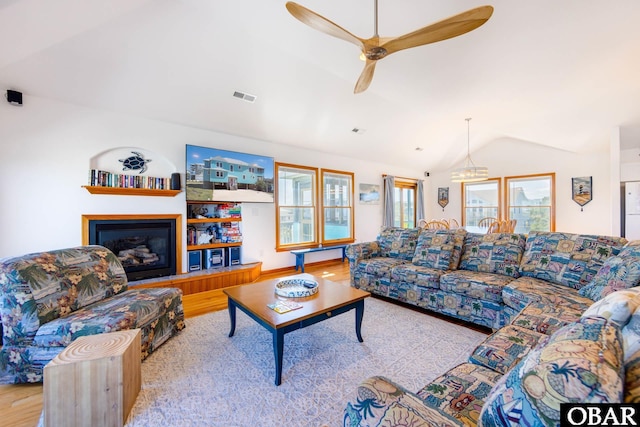 living area featuring visible vents, a ceiling fan, a glass covered fireplace, vaulted ceiling, and light wood-type flooring