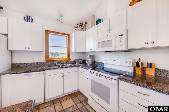 kitchen featuring white appliances, dark stone countertops, stone finish flooring, white cabinetry, and a sink