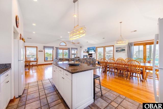 kitchen with dark stone counters, a kitchen island, freestanding refrigerator, a kitchen bar, and white cabinetry