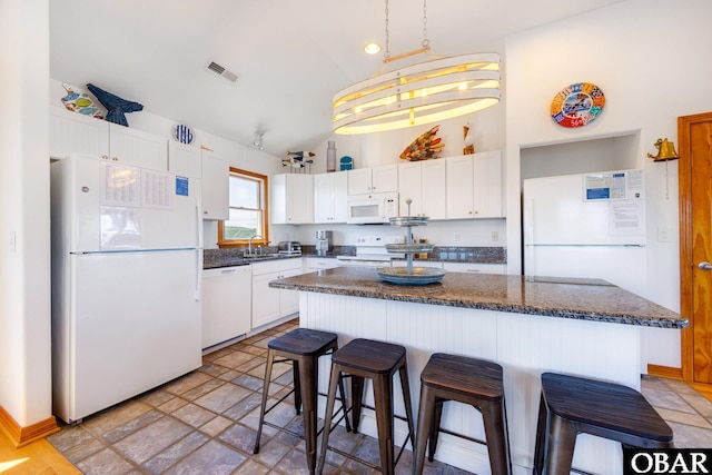 kitchen with a breakfast bar, visible vents, white cabinetry, a kitchen island, and white appliances