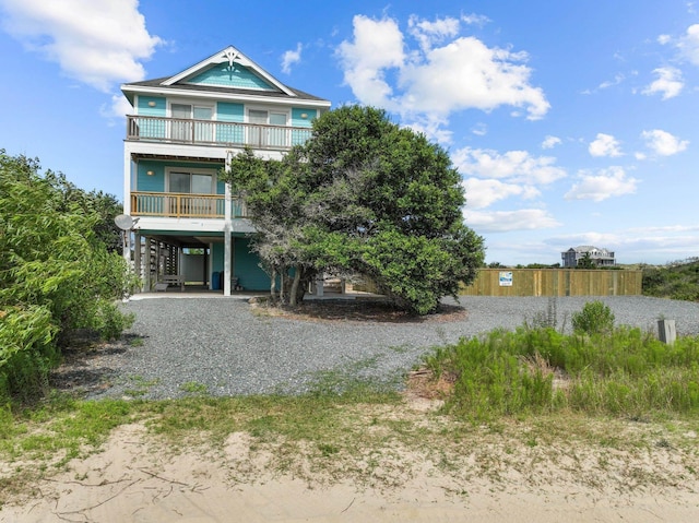 raised beach house featuring a carport, gravel driveway, and a balcony