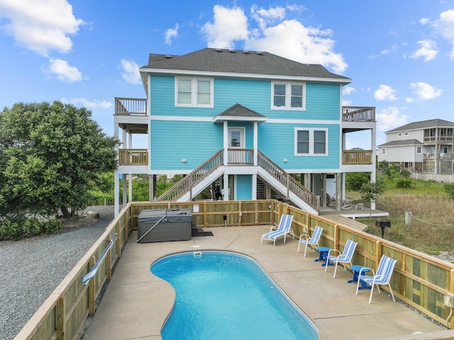 rear view of property featuring a fenced in pool, a hot tub, roof with shingles, a balcony, and a patio