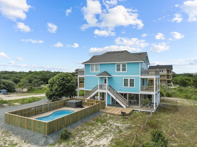 rear view of house featuring a wooden deck, a fenced in pool, a balcony, and roof with shingles