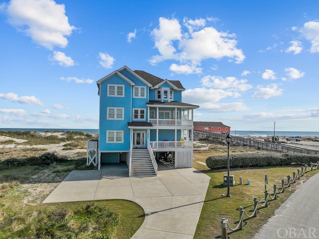 coastal inspired home featuring concrete driveway, a balcony, stairway, a water view, and a carport