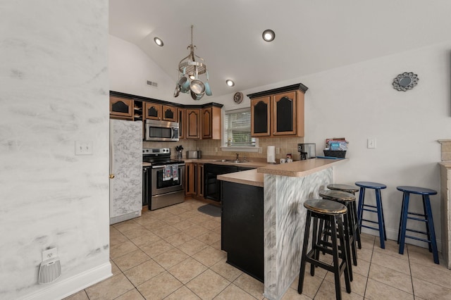 kitchen featuring a breakfast bar, stainless steel appliances, light countertops, glass insert cabinets, and a peninsula