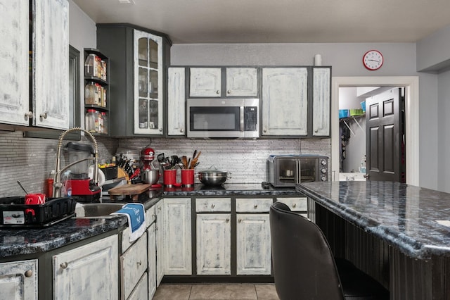 kitchen with a toaster, light tile patterned floors, stainless steel microwave, decorative backsplash, and glass insert cabinets