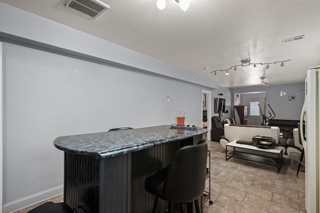 bar with a dry bar, visible vents, a textured ceiling, and freestanding refrigerator