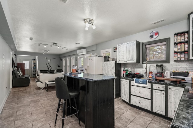 kitchen featuring a center island, visible vents, decorative backsplash, white fridge with ice dispenser, and a kitchen breakfast bar