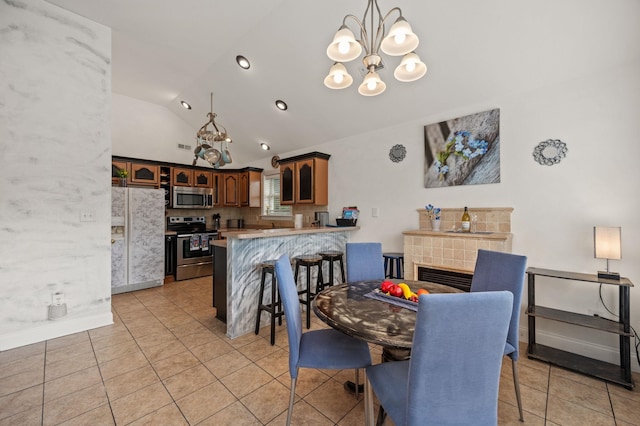 dining area with lofted ceiling, light tile patterned floors, a tile fireplace, a notable chandelier, and baseboards