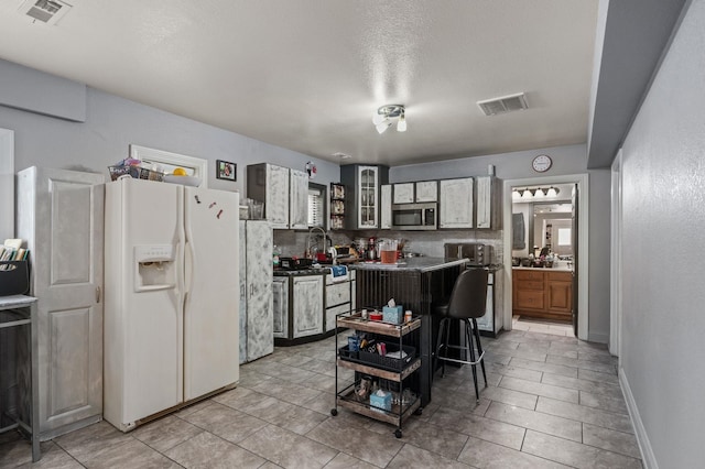 kitchen with white refrigerator with ice dispenser, stainless steel microwave, dark countertops, and visible vents