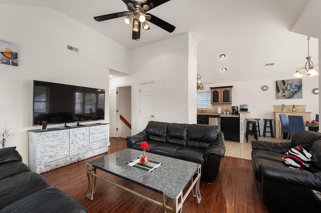 living area featuring dark wood-type flooring, visible vents, vaulted ceiling, and ceiling fan with notable chandelier