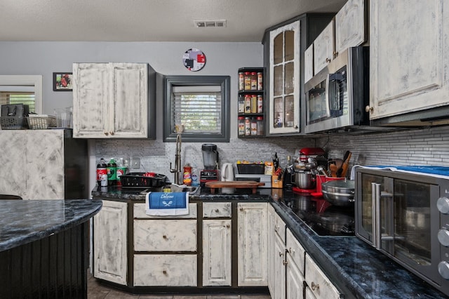 kitchen with tasteful backsplash, dark countertops, stainless steel microwave, glass insert cabinets, and black microwave