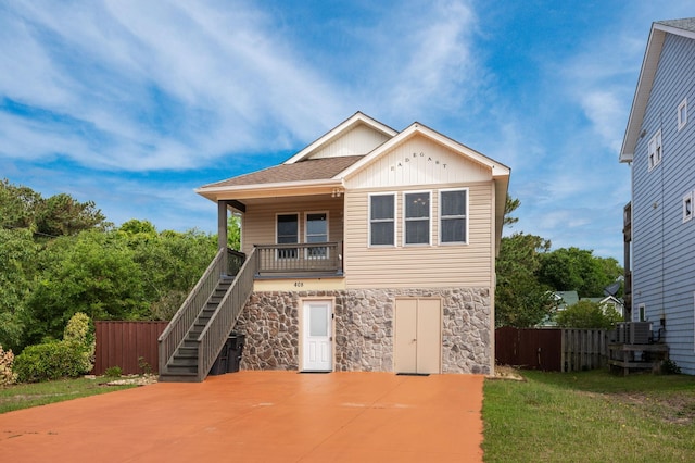 view of front of property with stairs, stone siding, a front yard, and fence