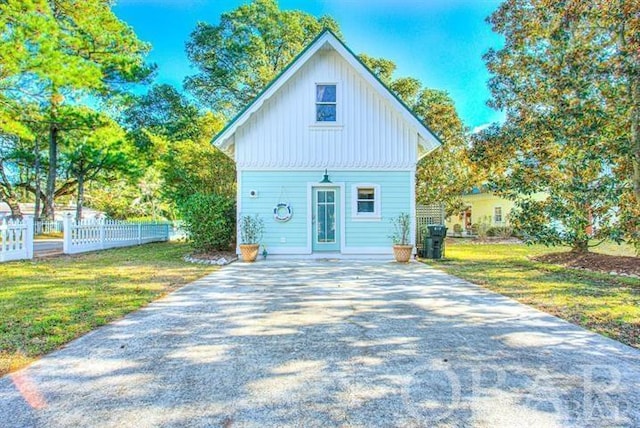 view of front of home featuring board and batten siding, fence, and a front lawn