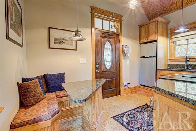 kitchen featuring dark stone countertops, freestanding refrigerator, hanging light fixtures, and a sink