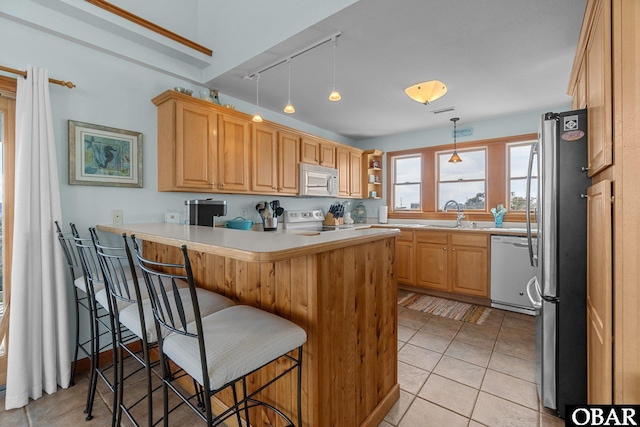 kitchen featuring a kitchen bar, a peninsula, light tile patterned flooring, white appliances, and a sink