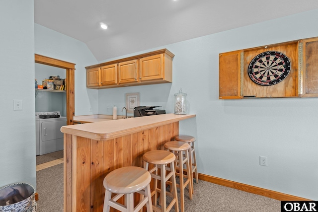 kitchen with a kitchen bar, washer and clothes dryer, baseboards, light countertops, and lofted ceiling