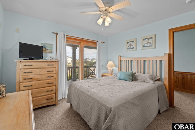 carpeted bedroom featuring a wainscoted wall, wood walls, a ceiling fan, and access to outside