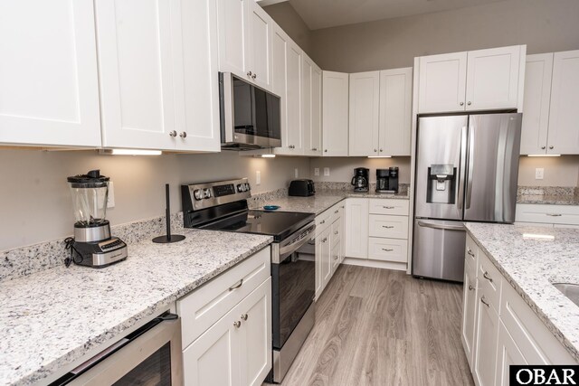 kitchen with light stone counters, appliances with stainless steel finishes, light wood-style flooring, and white cabinetry