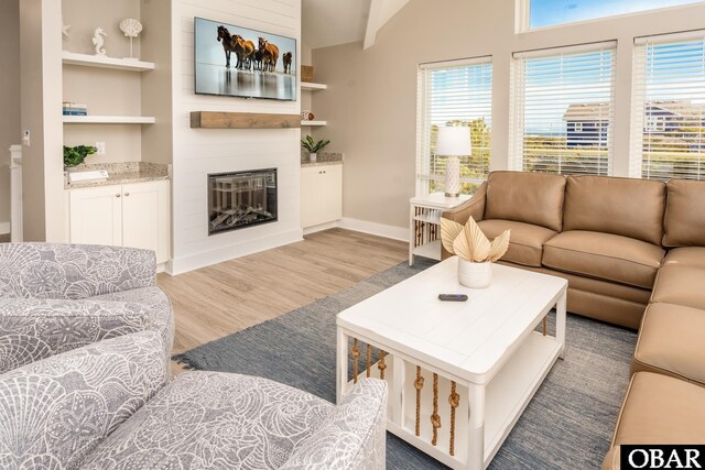 living room featuring light wood-style floors, a large fireplace, baseboards, and built in features