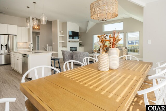 dining area featuring light wood-type flooring, vaulted ceiling, a fireplace, and an inviting chandelier