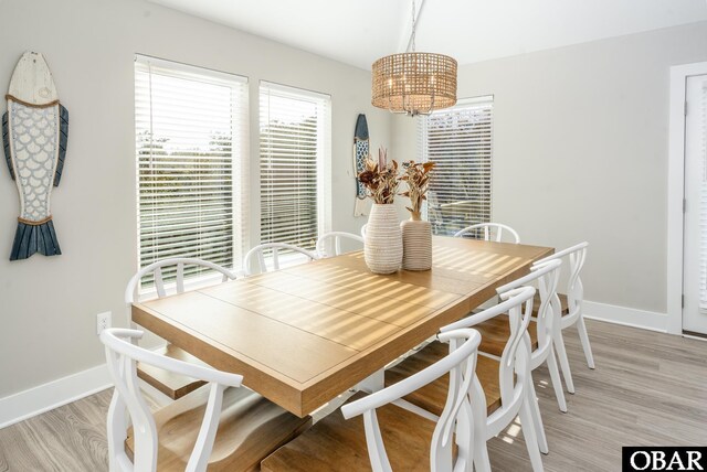 dining space with light wood-type flooring, a notable chandelier, and baseboards