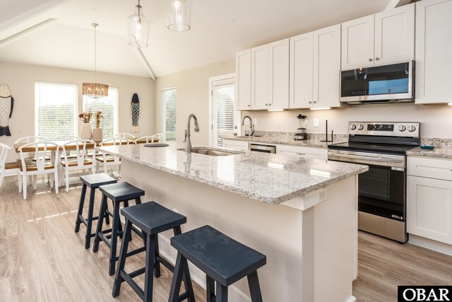 kitchen featuring a kitchen island with sink, a sink, white cabinetry, hanging light fixtures, and appliances with stainless steel finishes