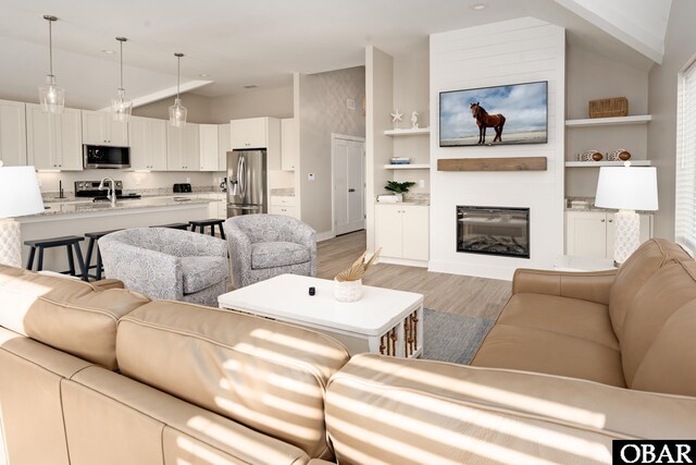 living area with vaulted ceiling, built in shelves, light wood-type flooring, and a glass covered fireplace