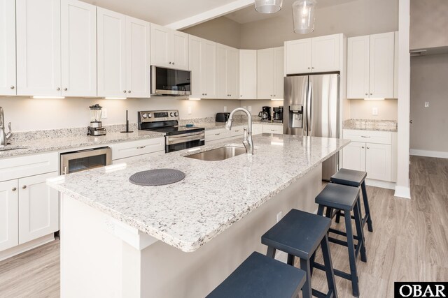 kitchen featuring stainless steel appliances, white cabinetry, a sink, an island with sink, and light stone countertops