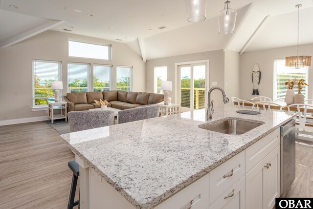 kitchen with white cabinets, light stone counters, open floor plan, hanging light fixtures, and a sink